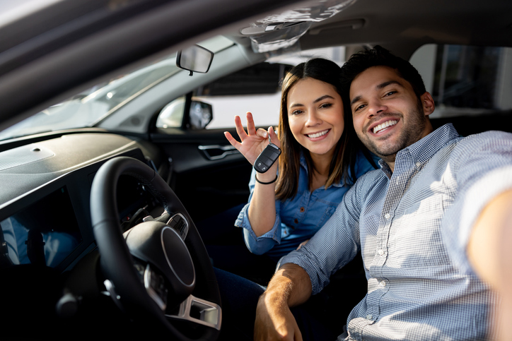 Happy couple buying a new car and sitting in it holding the keys and smiling at the camera